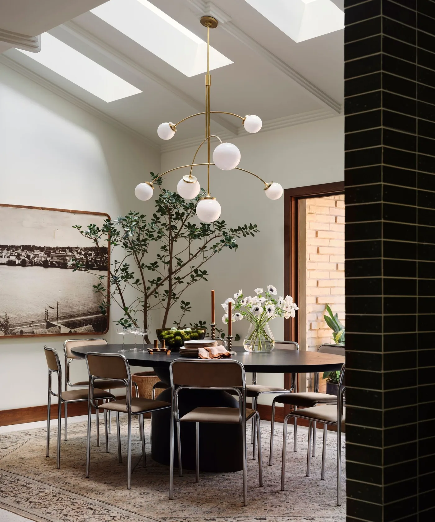 Dining room with a dark oval table, brown chairs, patterned pale rug, skylights and a sculptural pendant.