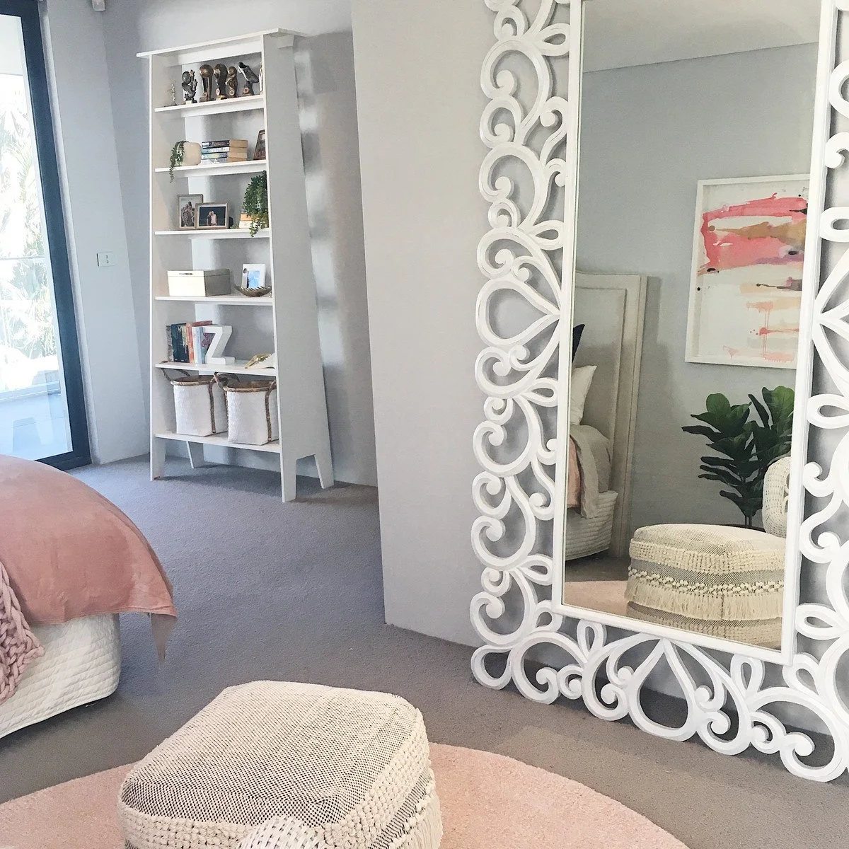 Teen bedroom with an ornate white floor mirror, narrow open shelving and pale pink bedding