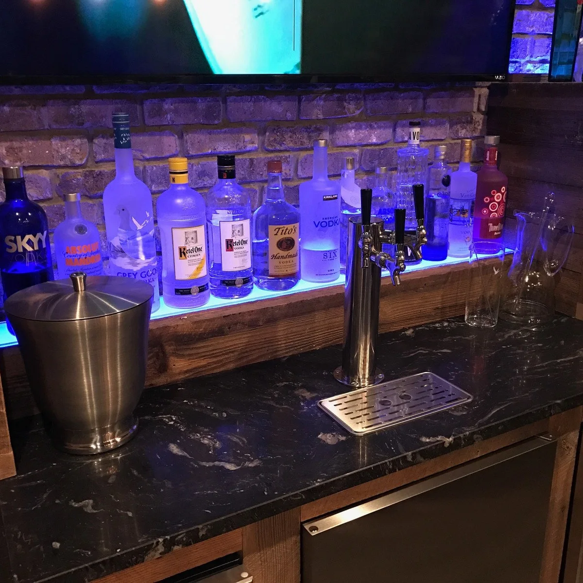 Close basement bar view with illuminated bottles, draft tap and dark patterned counter
