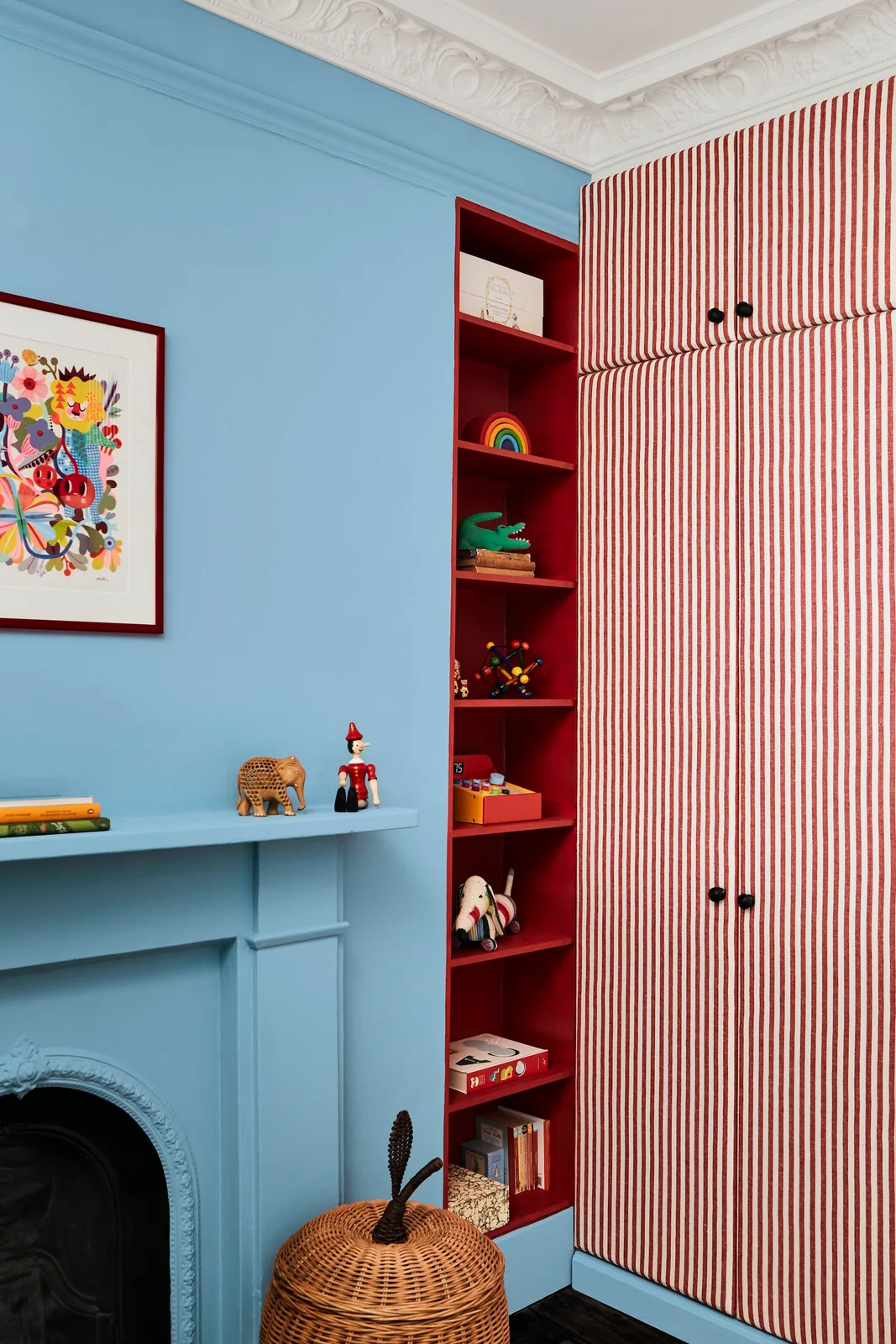 Red open shelves beside striped wardrobe doors displaying a small selection of toys and books