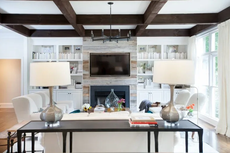 White shelves and lower cupboards beside pale textured fireplace wall and television under dark beams