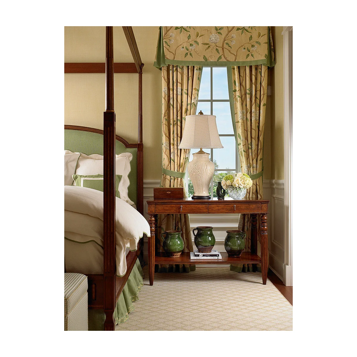Wood-colored console beside a four-poster bed with green-trimmed bedding and floral curtains