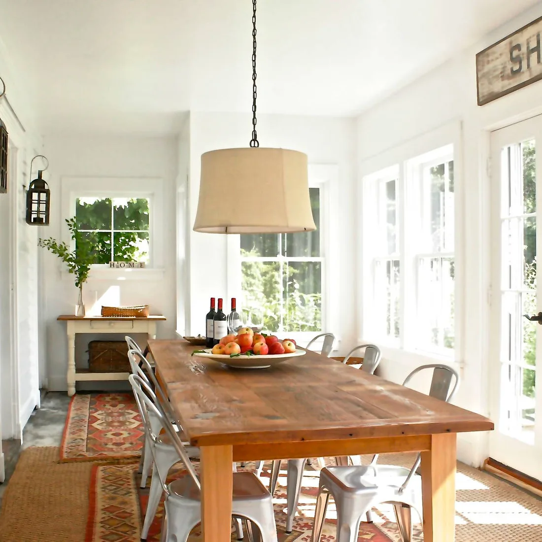 Rustic wood dining table and metal chairs over a textured neutral rug with a narrow red patterned rug