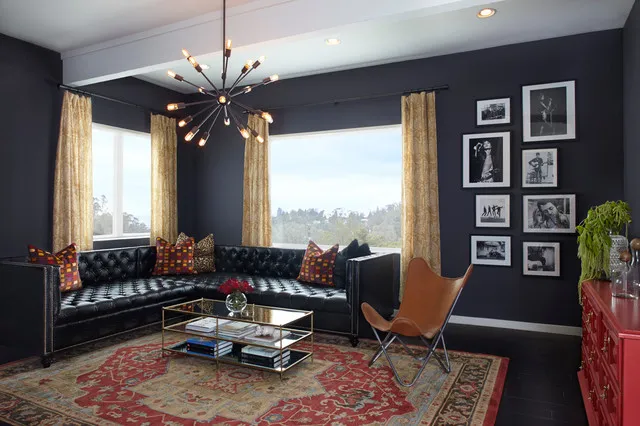 A dark tufted sofa sits against deep walls beside warm pale curtains and a patterned rug.