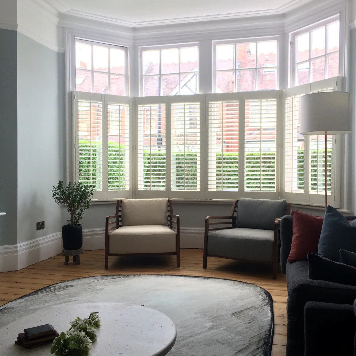 Two wood-framed chairs below half-height shutters in a pale blue terrace living room