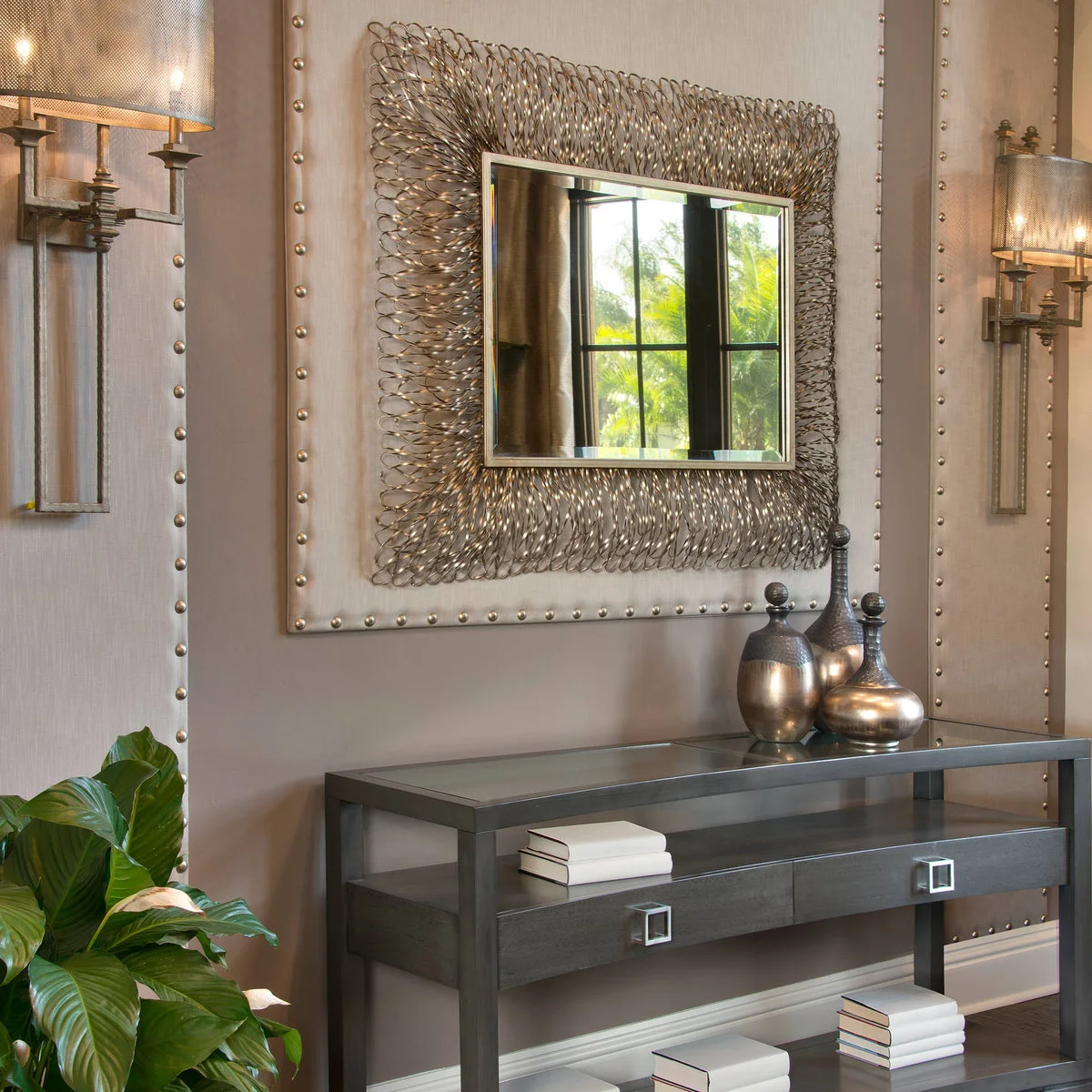 A dark open console with three metallic decorative vessels at one end beneath a textured mirror.