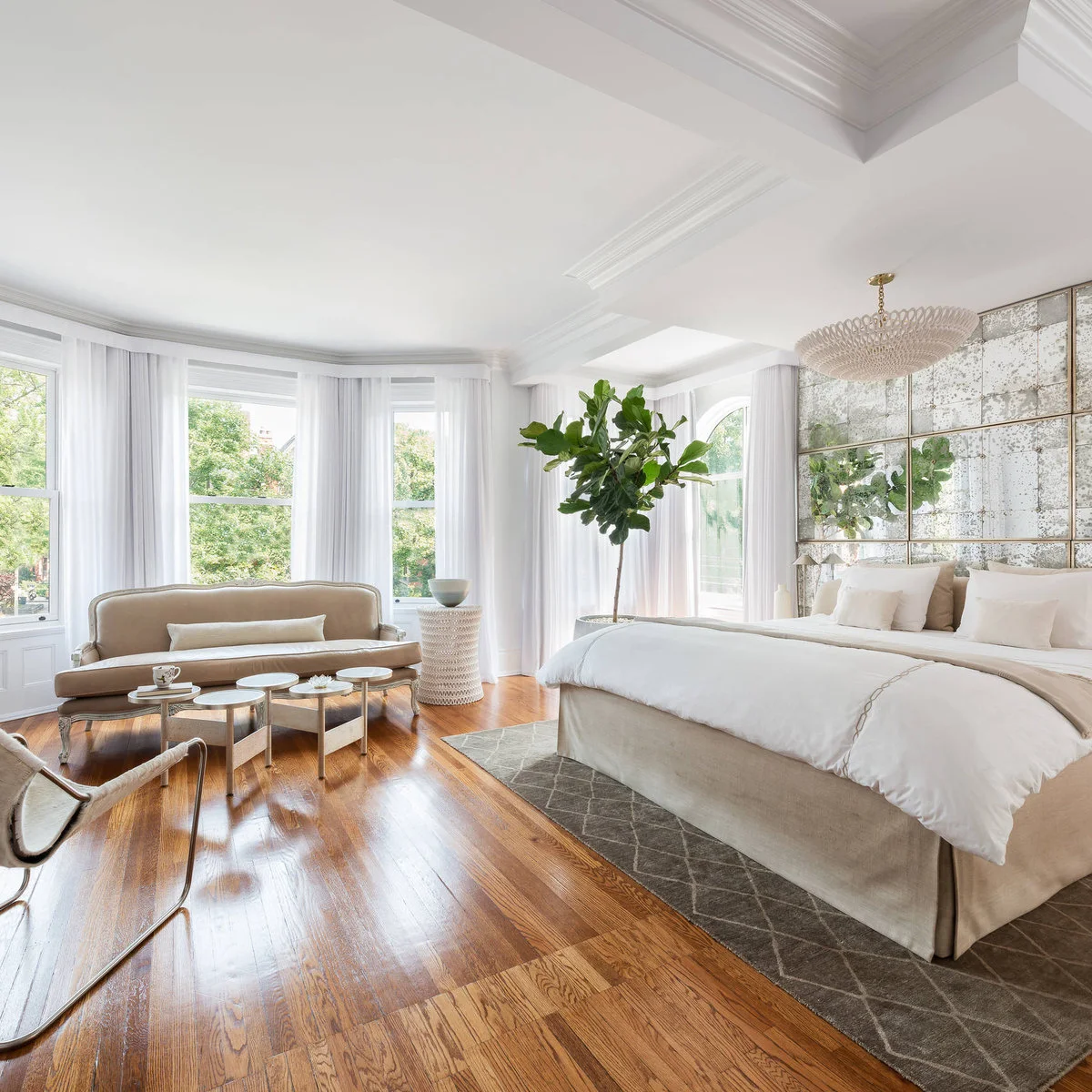 Bright bedroom with curved beige settee, pale bedding and a mottled mirror wall behind the bed