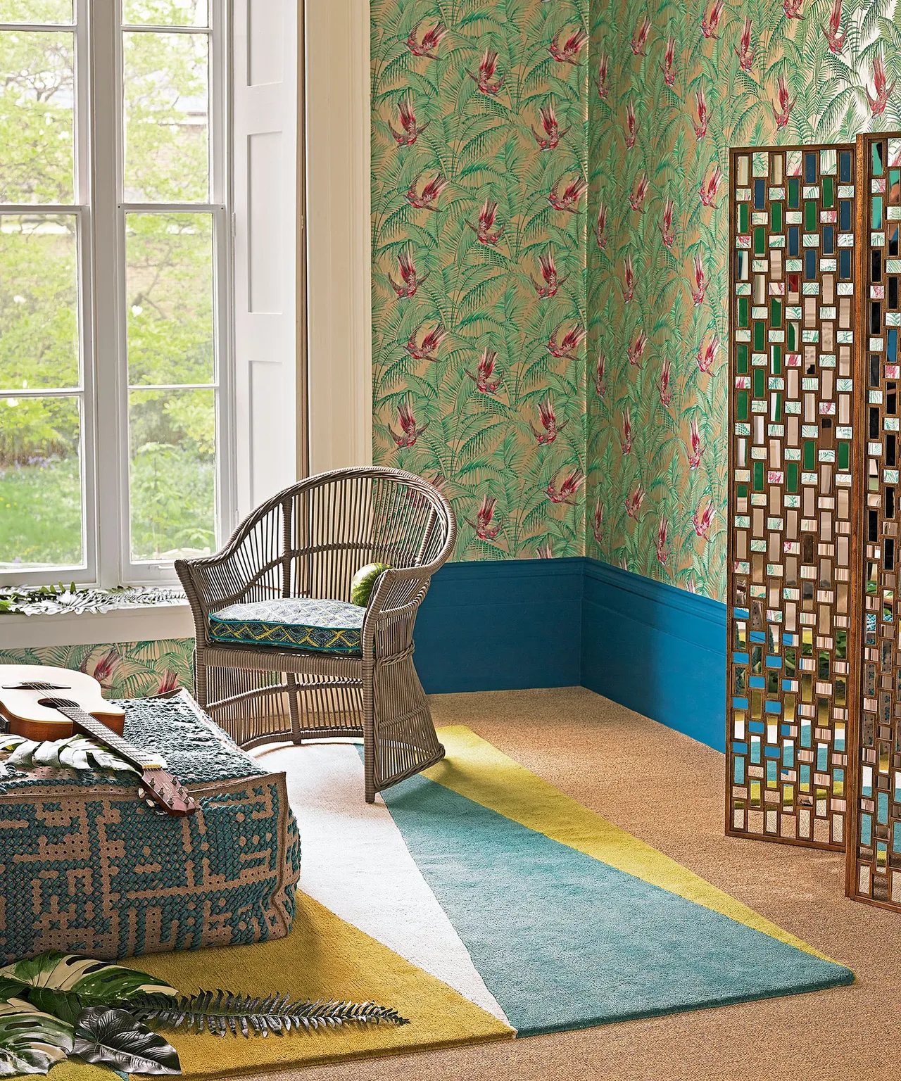 Sitting corner with green botanical and bird-patterned wall, teal lower wall, woven chair, decorative folding screen and green-and-yellow rug.