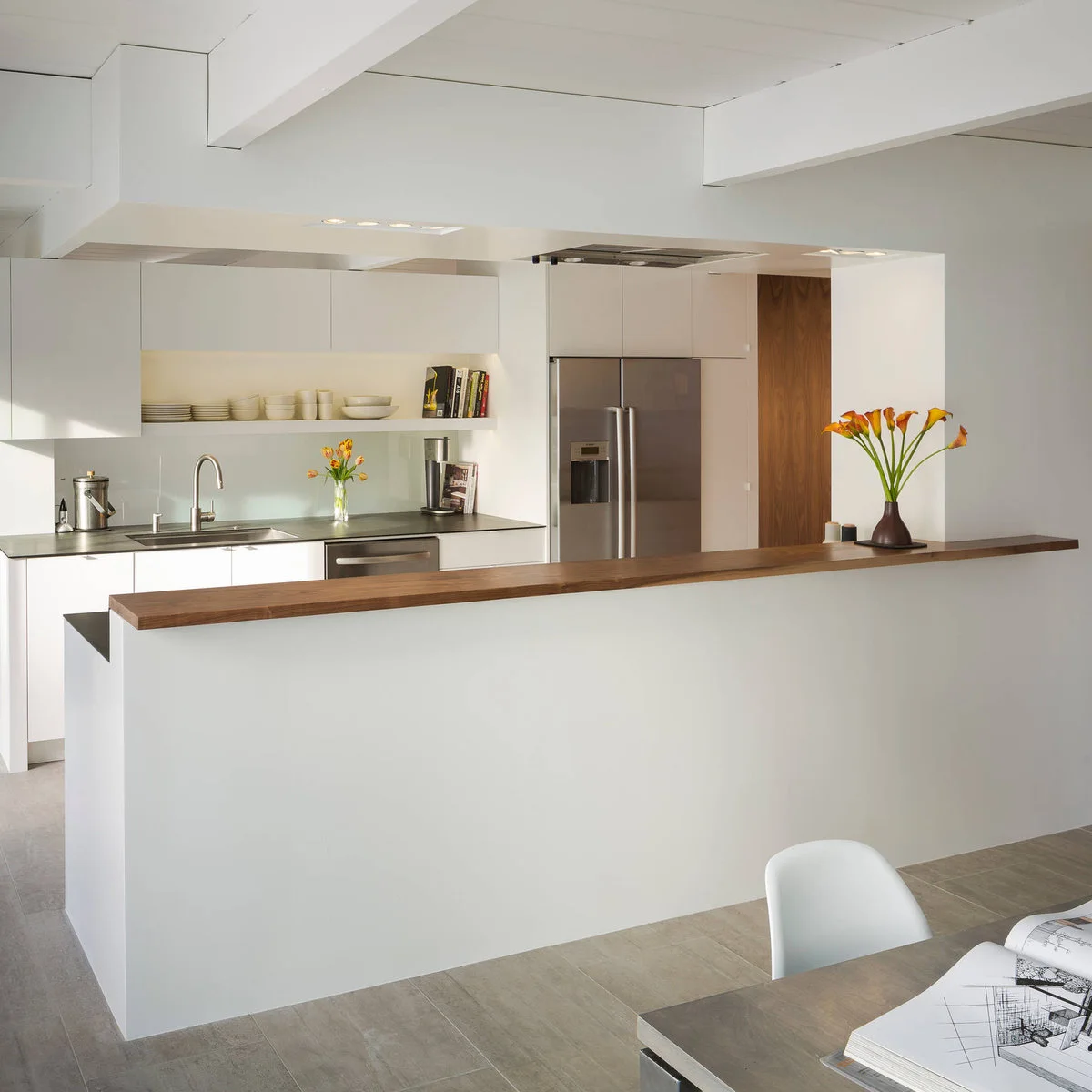 A white half wall with a narrow wood cap screens a white kitchen from the dining area.