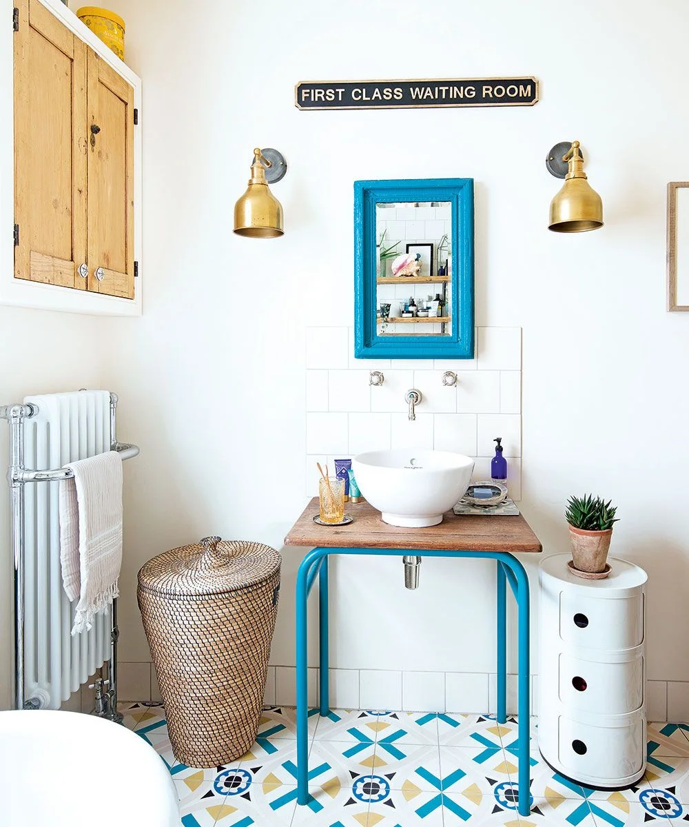 White vessel basin on a wood-topped blue metal table with a matching blue mirror and nearby compact storage.