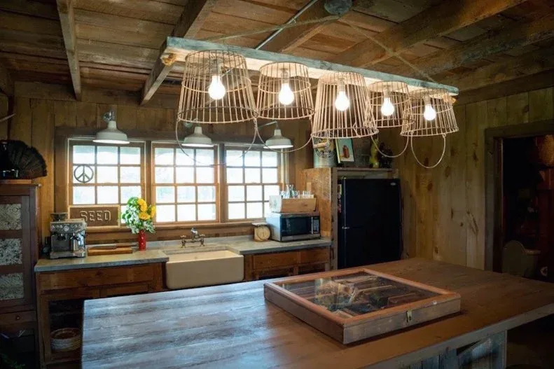 Wood-clad walls and ceiling surround a broad wooden island, apron-front sink and basket-shaped hanging shades beside windows and countertop appliances