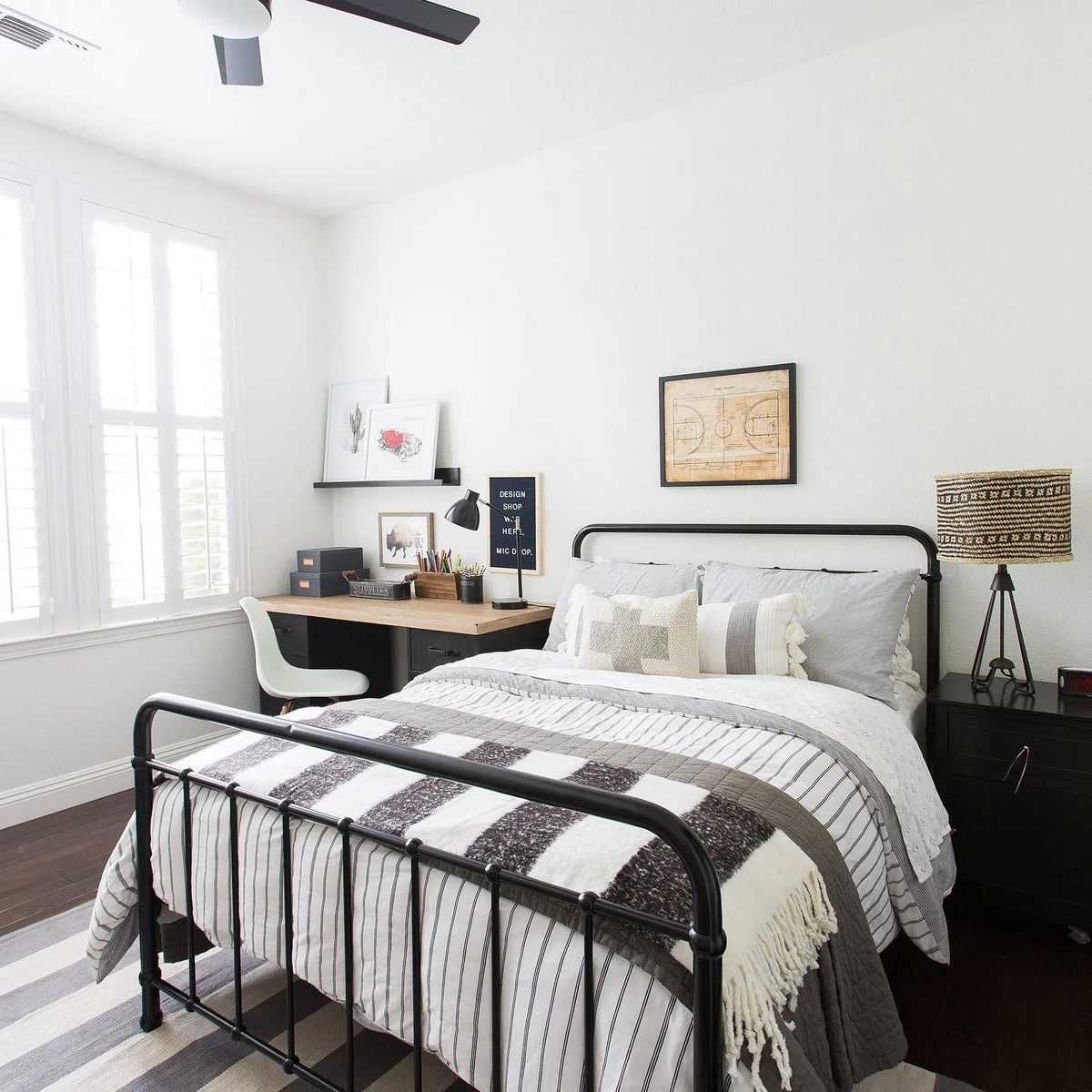 White teen bedroom with black metal-looking bed, wood-colored desk and a white chair