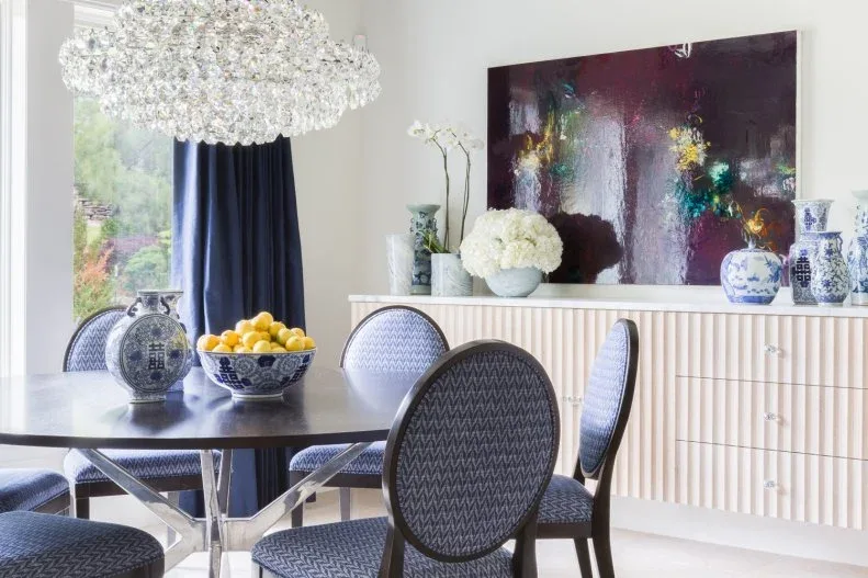 Blue-and-white vase and matching bowl of yellow fruit on a dark round table with blue oval-back chairs