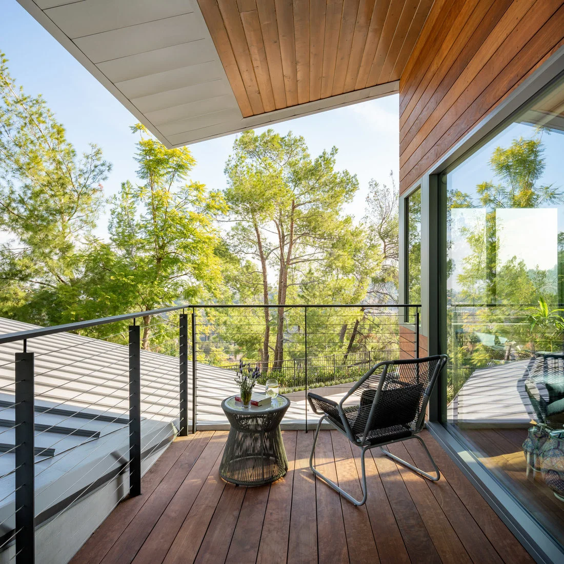 A dark woven chair and small round table sit beside glass doors on a timber-floored balcony