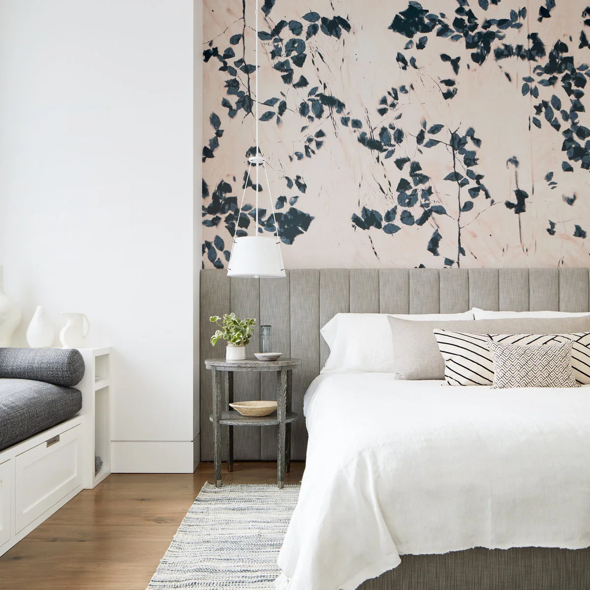 Dark leafy wallpaper on a pale background above a tall gray paneled headboard beside a white pendant light.