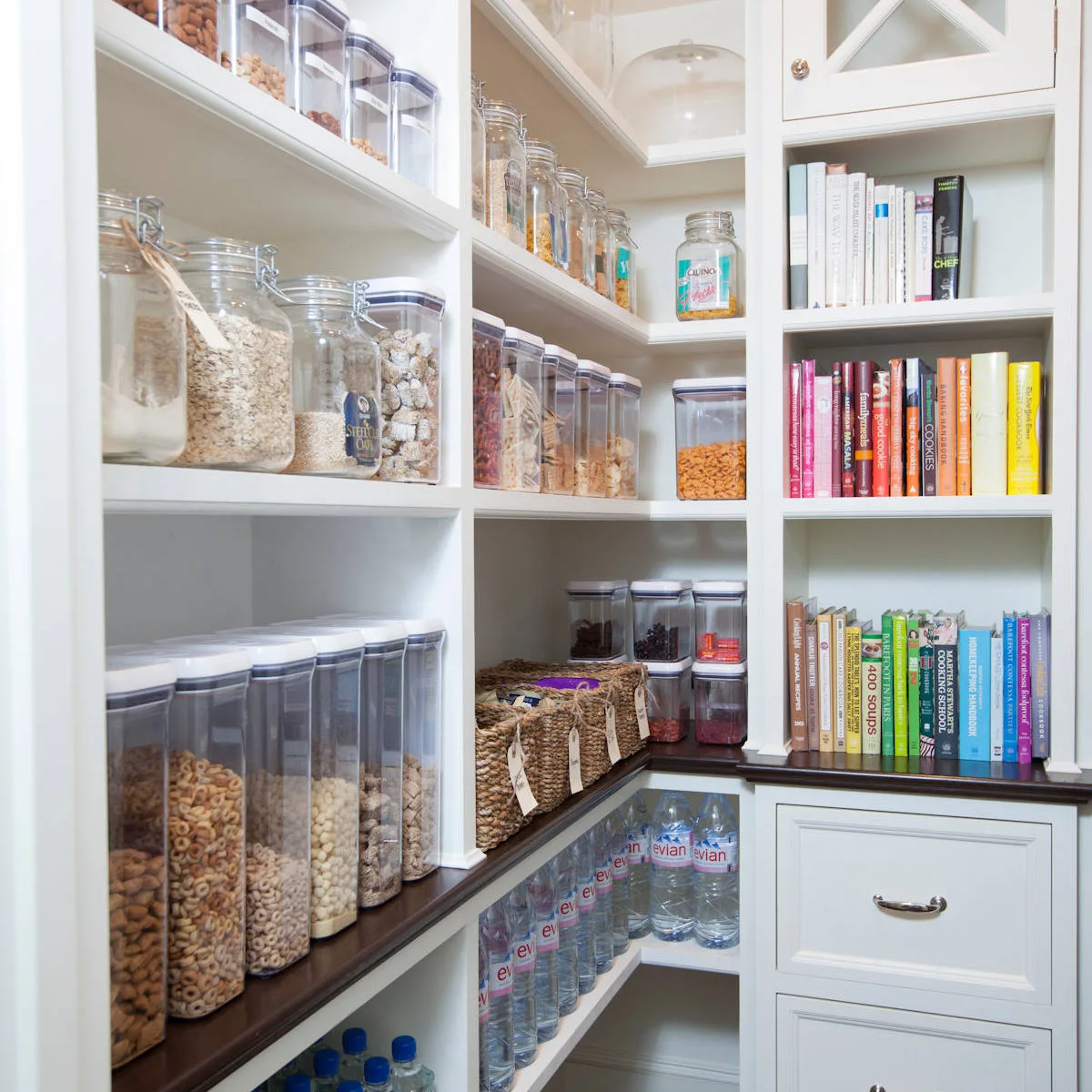 White pantry corner with food containers beside a narrow shelf column of cookbooks
