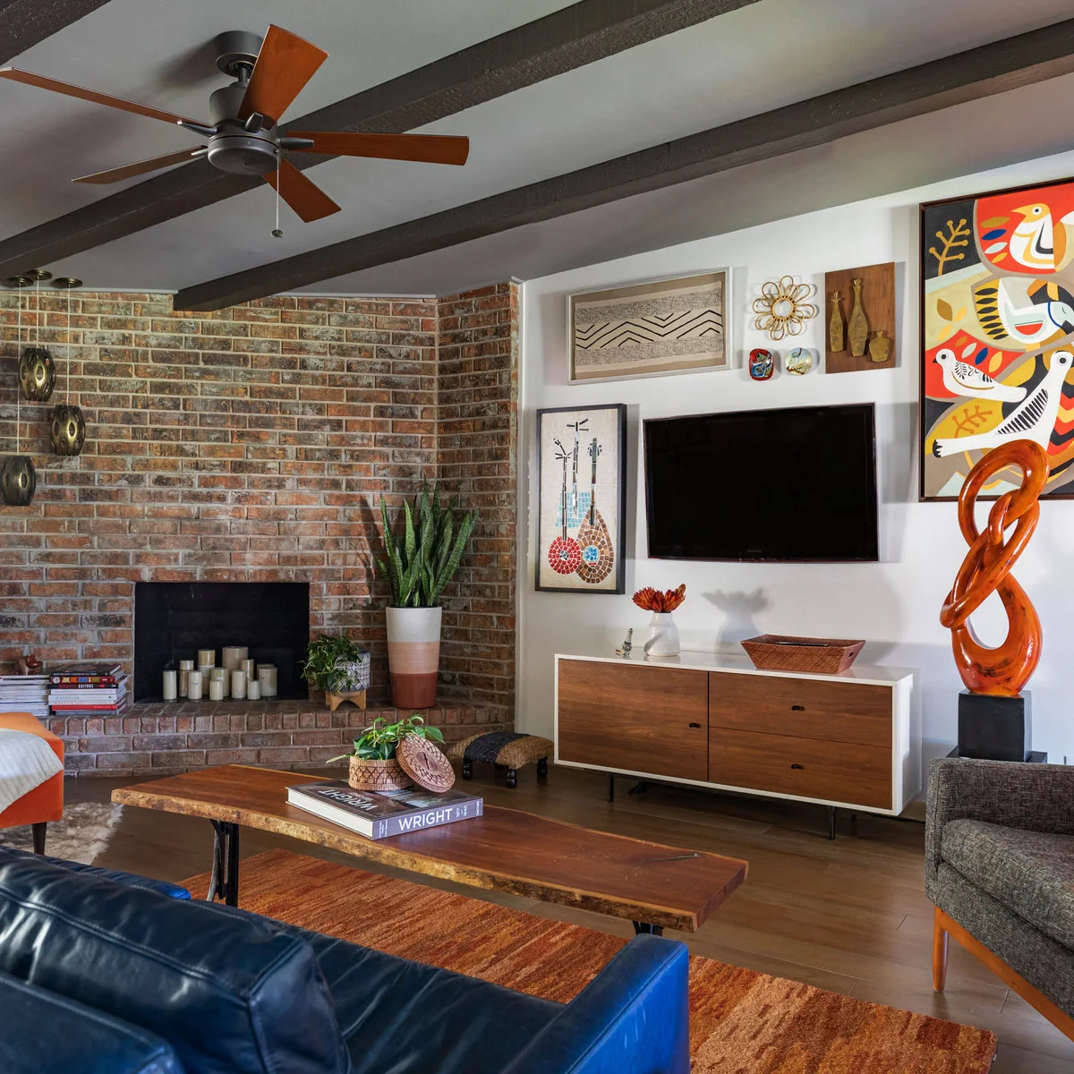 Long framed print and small sculptural wall pieces above a television beside colorful bird art and a brick fireplace.