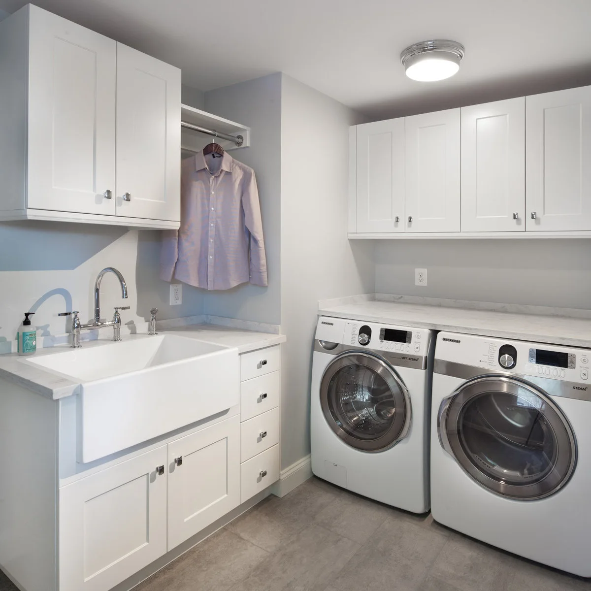 White laundry room with an apron-front sink, a short shirt rail and silver machines under a separate counter