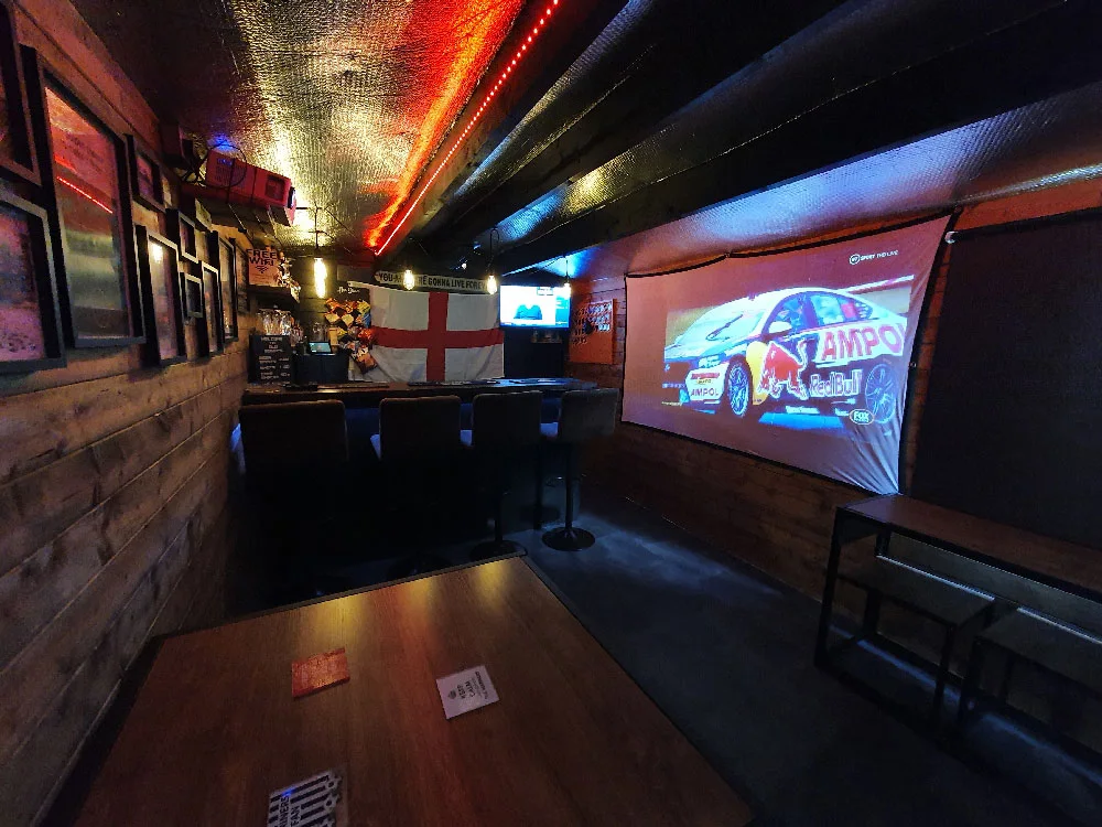 Long timber shed pub with a projection screen on the side wall and a bar at the far end