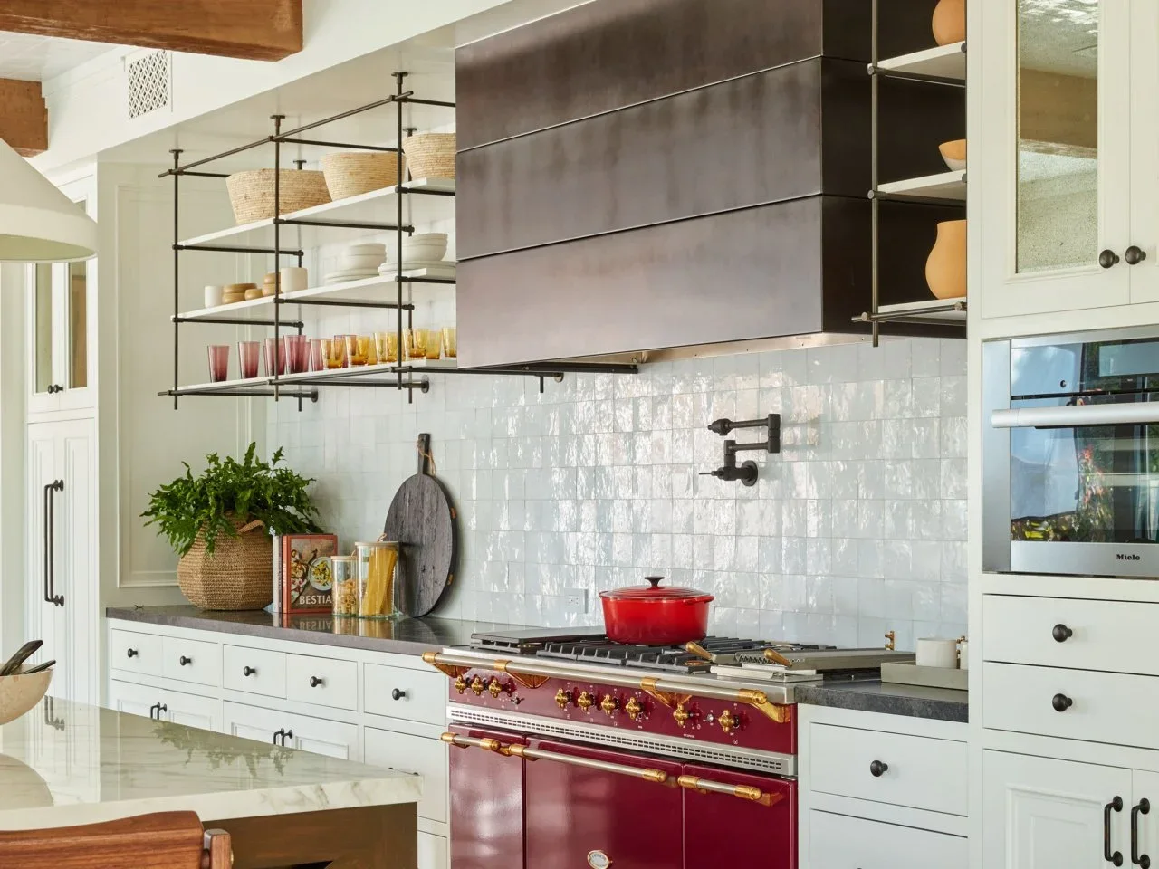 Glossy white square backsplash tiles sit behind a red range beneath a dark hood beside open metal-framed shelves.