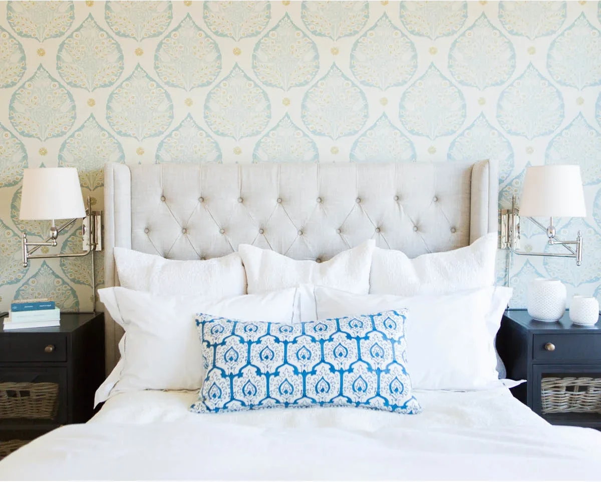 Two pale shaded metal swing-arm wall lights flank a broad white tufted winged headboard above dark nightstands.