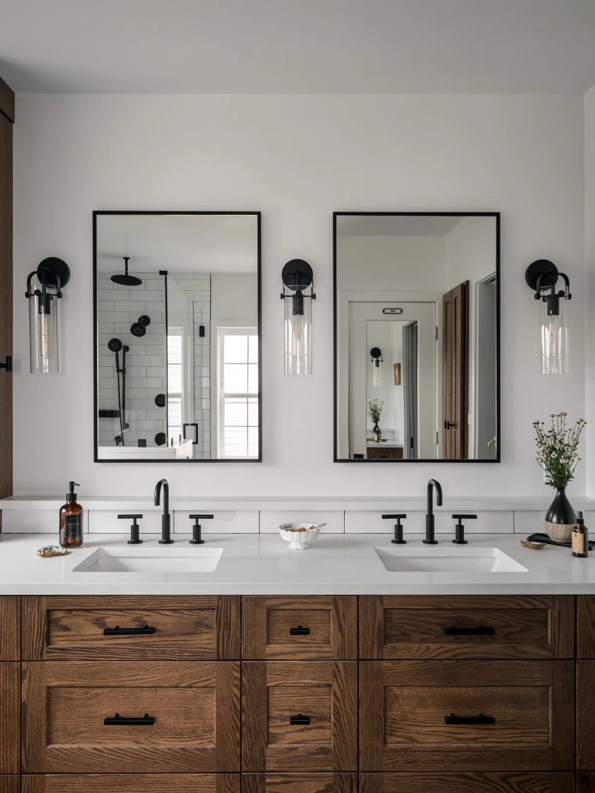 A double wood vanity with a white counter sits beneath two black rectangular mirrors and three glass wall lights.