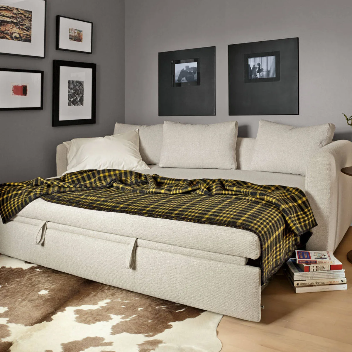 Cream sofa bed opened beneath black-framed pictures with a yellow plaid blanket