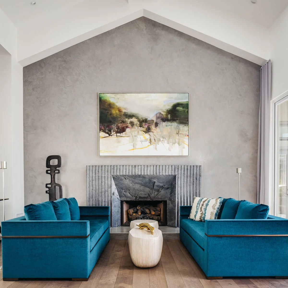 Two teal sofas face one another beneath a tall textured gray wall and gray fireplace surround.