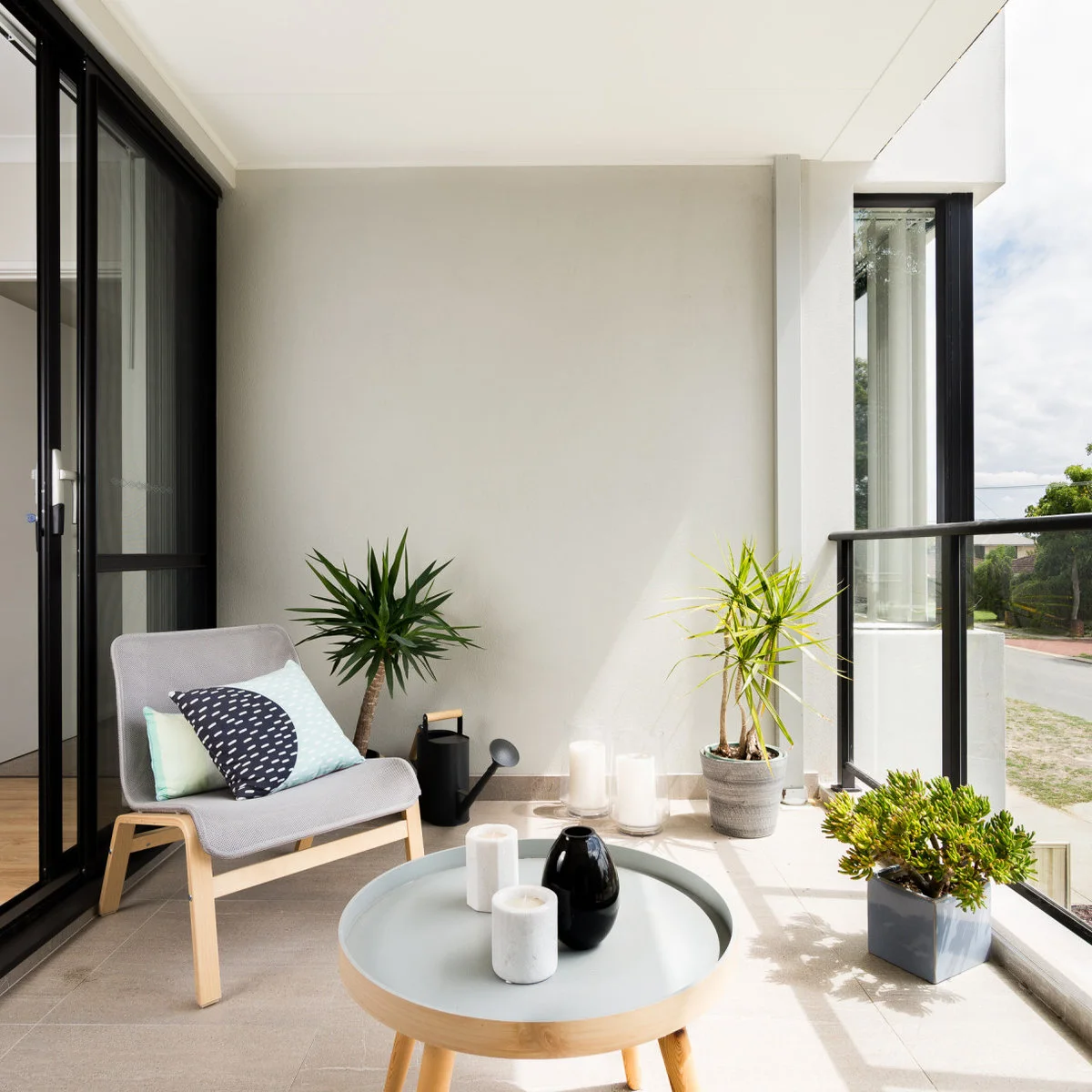 Pale apartment balcony with one chair, round table and several potted plants