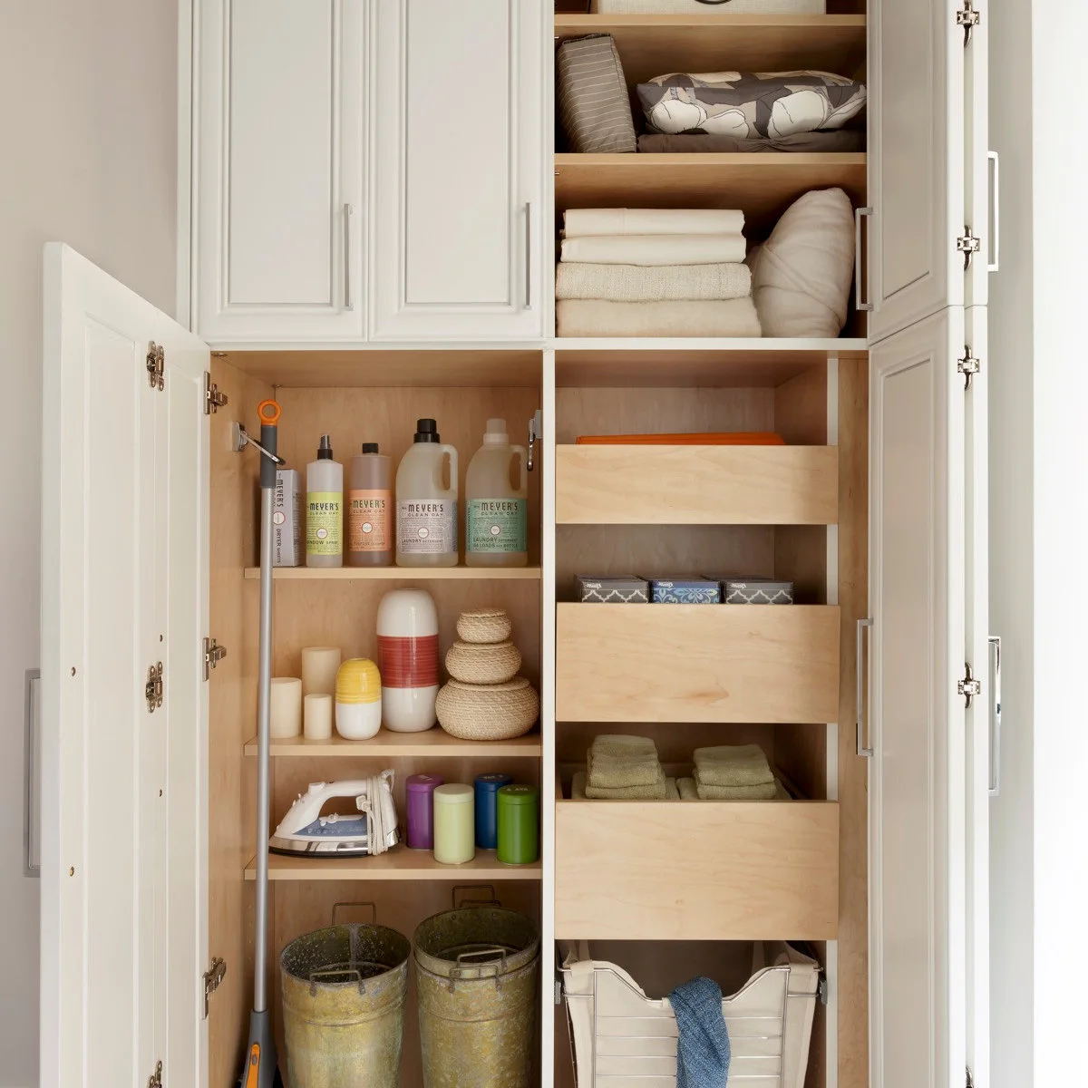 Tall white utility cabinet with folded towels and bedding on one side and cleaning supplies on the other