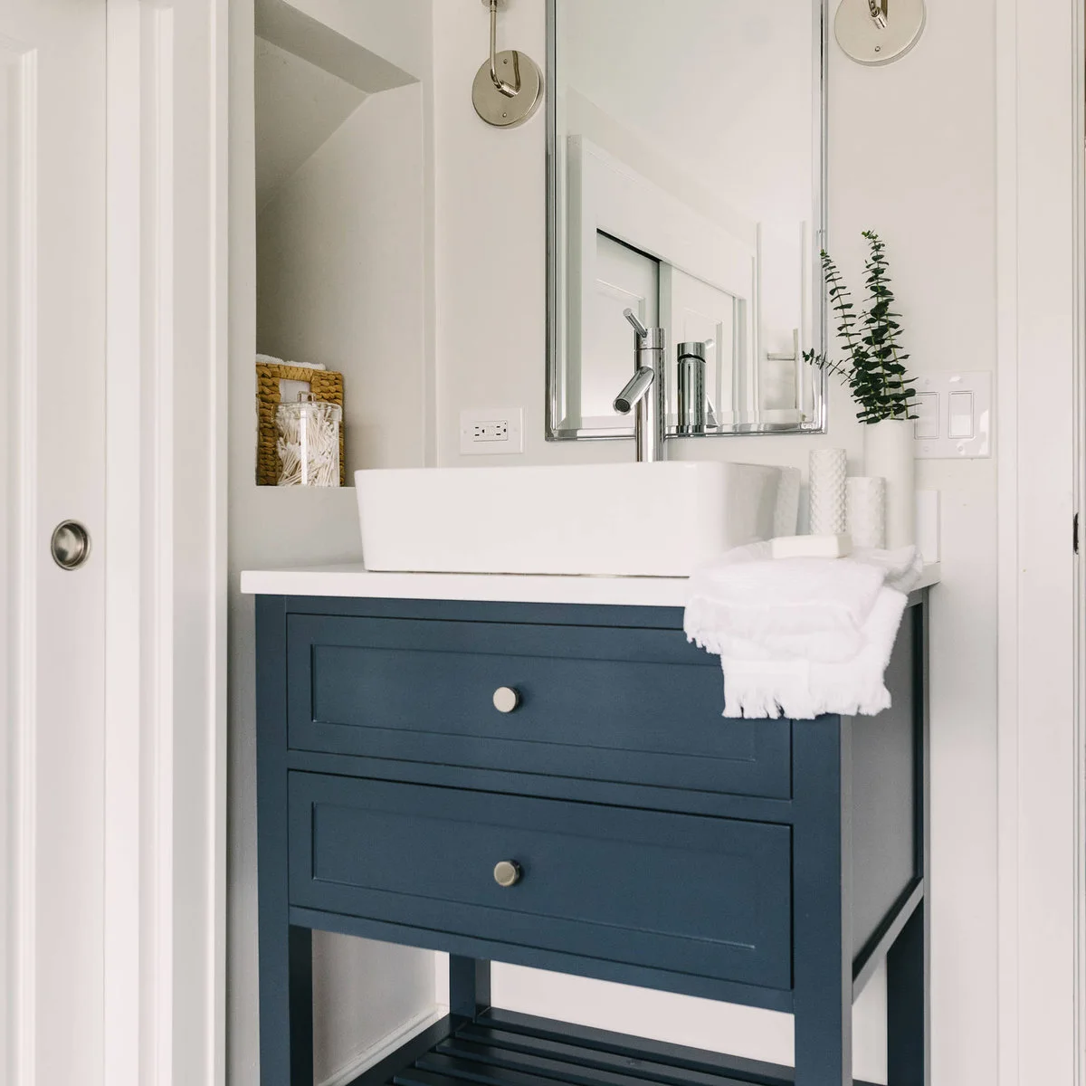 A tall white rectangular vessel sink sits on a navy freestanding vanity with drawers beside a recessed storage niche.