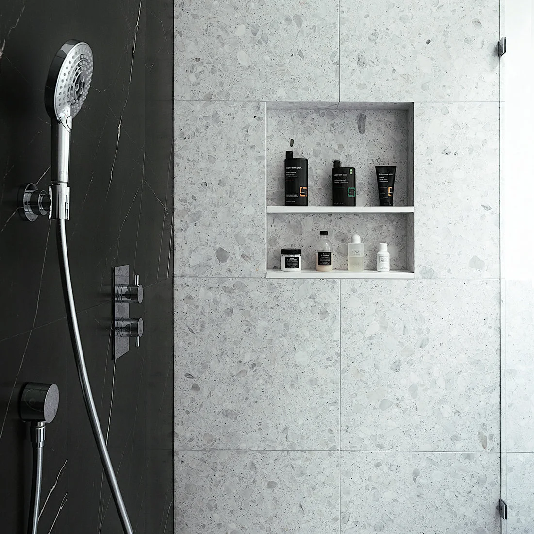 Pale chipped tile continues into a shower niche beside a dark veined wall and chrome fittings.