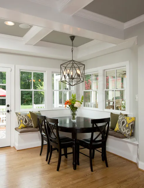 A dark curved table sits within a pale corner banquette beneath broad windows.