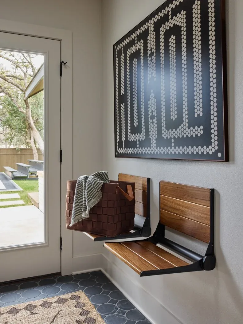Two wooden fold-down wall seats beneath large artwork beside a glass exterior door and a dark tiled floor.