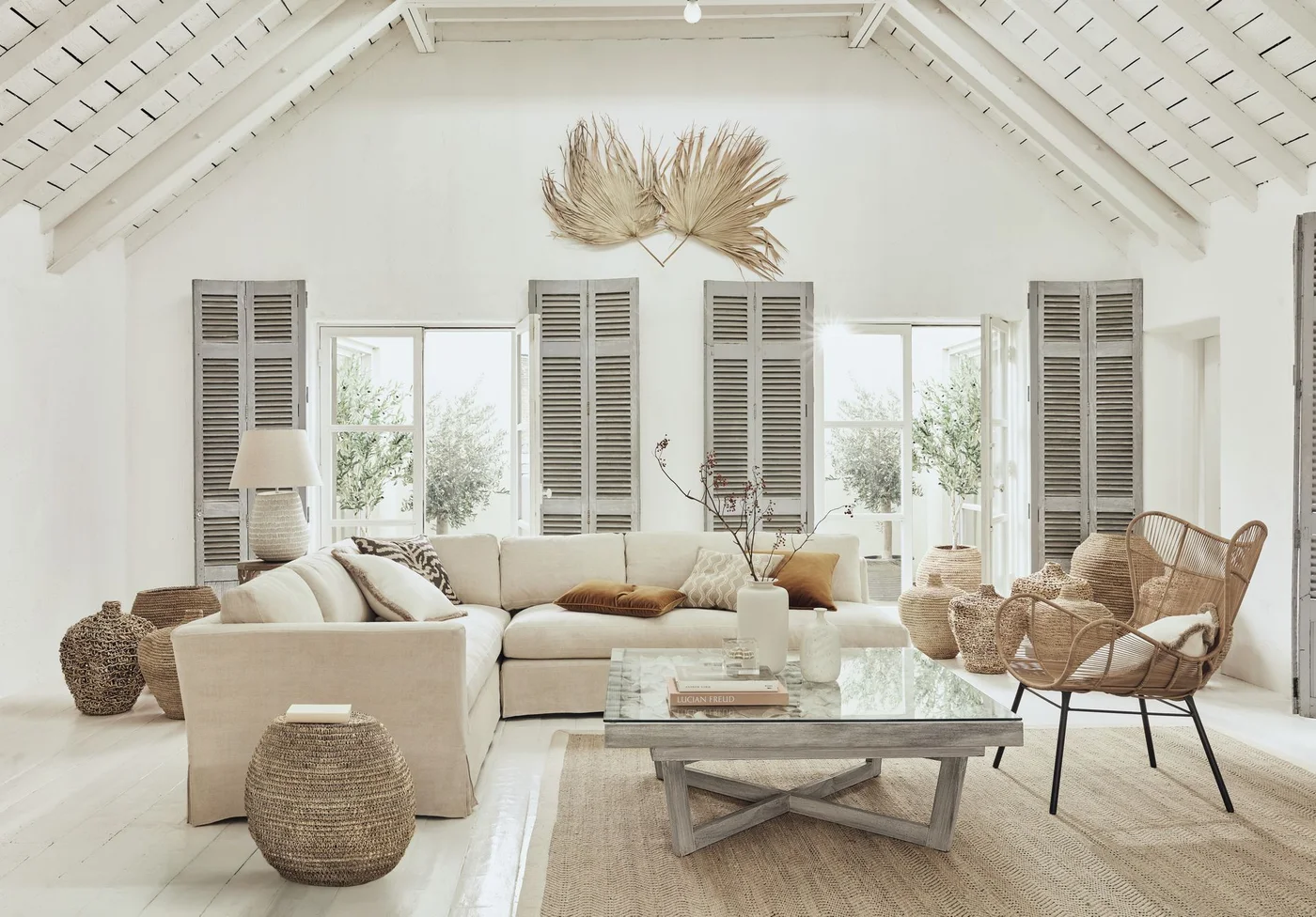 Glass-topped coffee table with books and a white branch vase beside woven seating