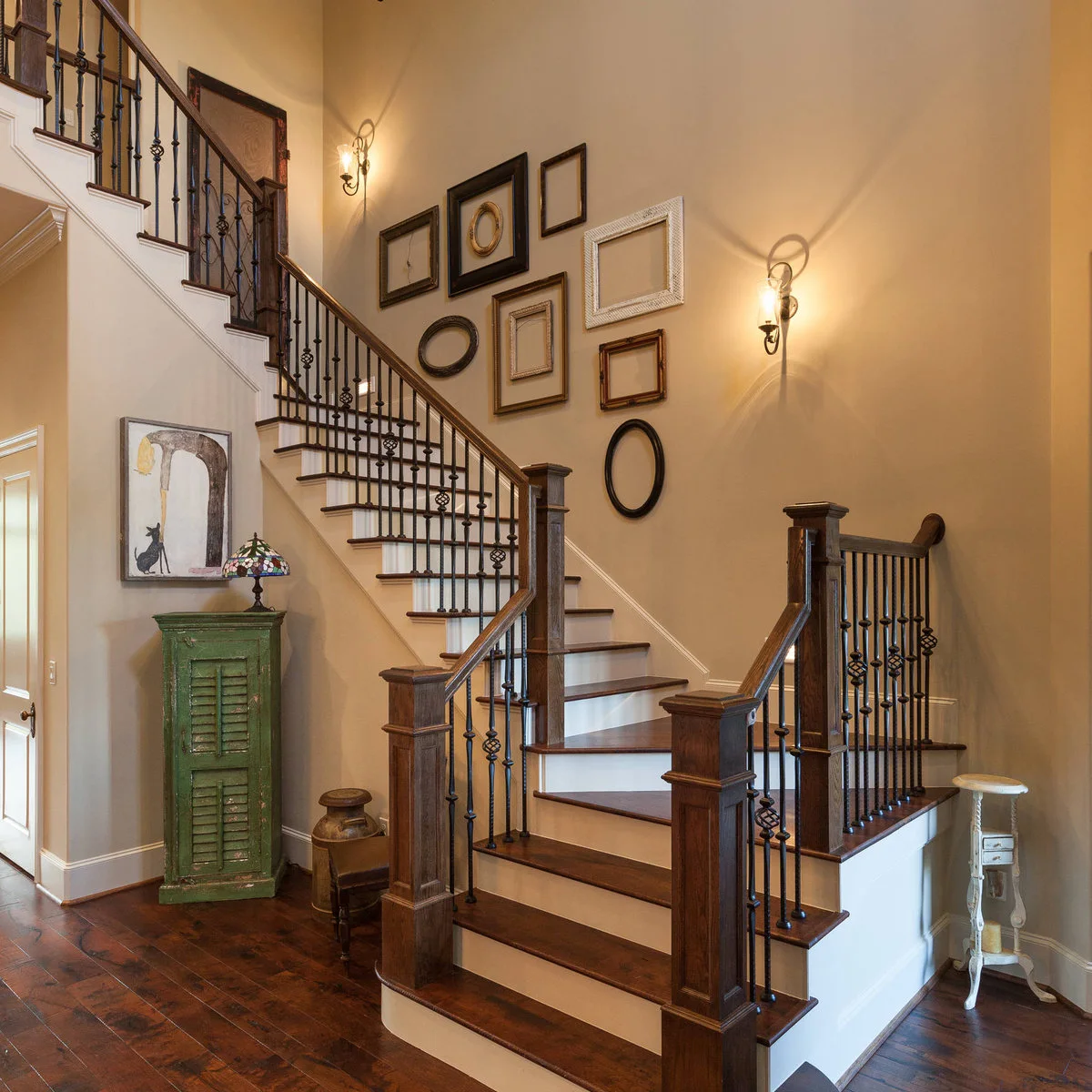 Traditional staircase with dark railings and a grouping of empty decorative frames on a warm wall