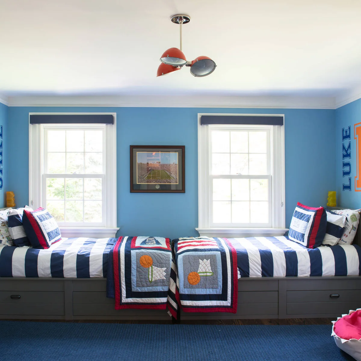 Two built-in beds placed end to end beneath windows with blue striped bedding and sports quilts