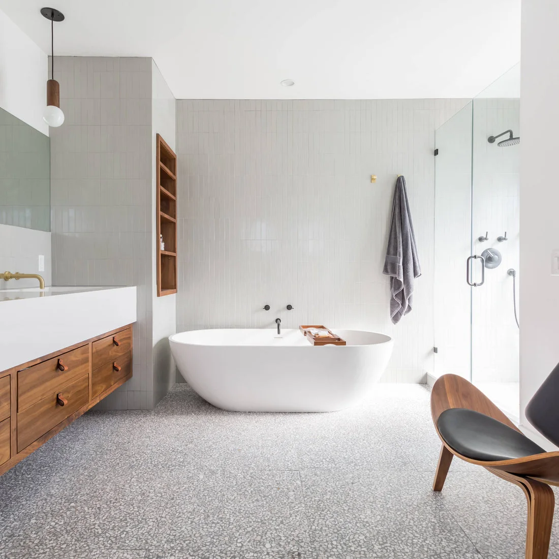 Fine gray terrazzo covers the floor beneath a white tub, timber vanity and pale wall tiles.