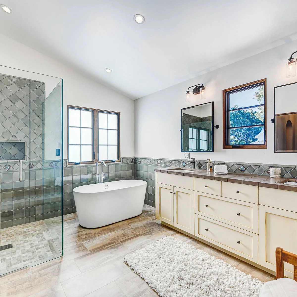 Bathroom with muted green square tiles, diamond-set border accents, pale vanity and white freestanding tub