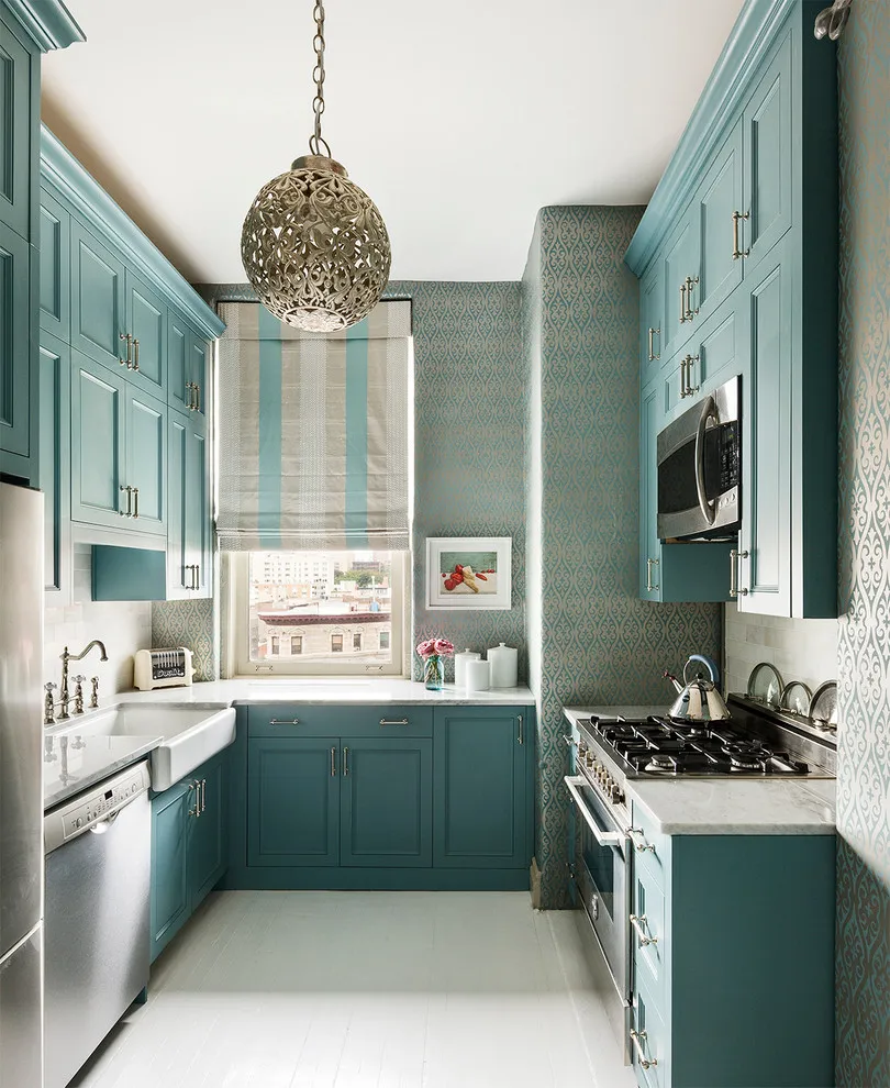 Teal cabinets line both sides of a narrow kitchen beneath a decorative pendant