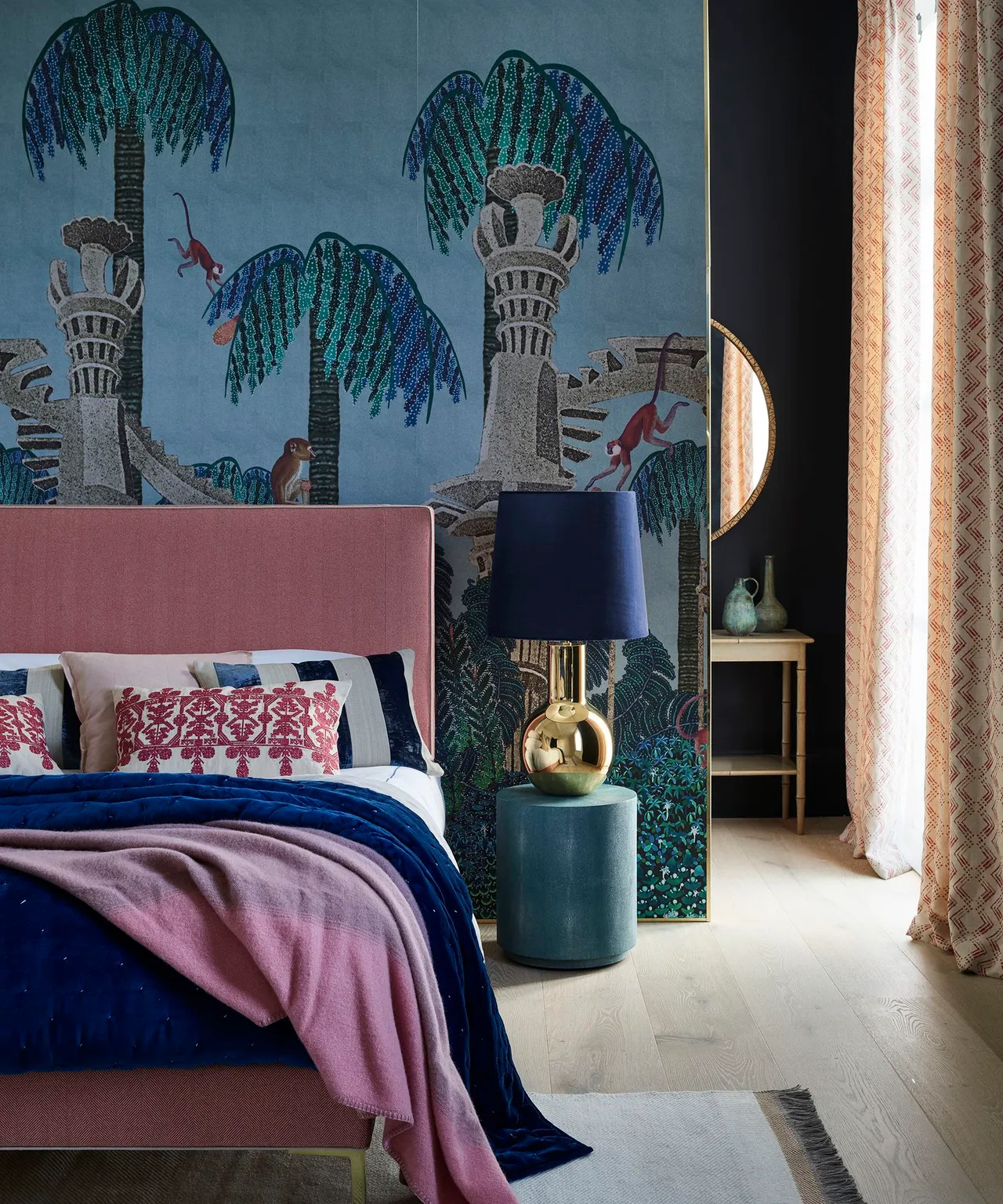 A blue scenic wall sits behind a pink upholstered bed and warm bedding accents.