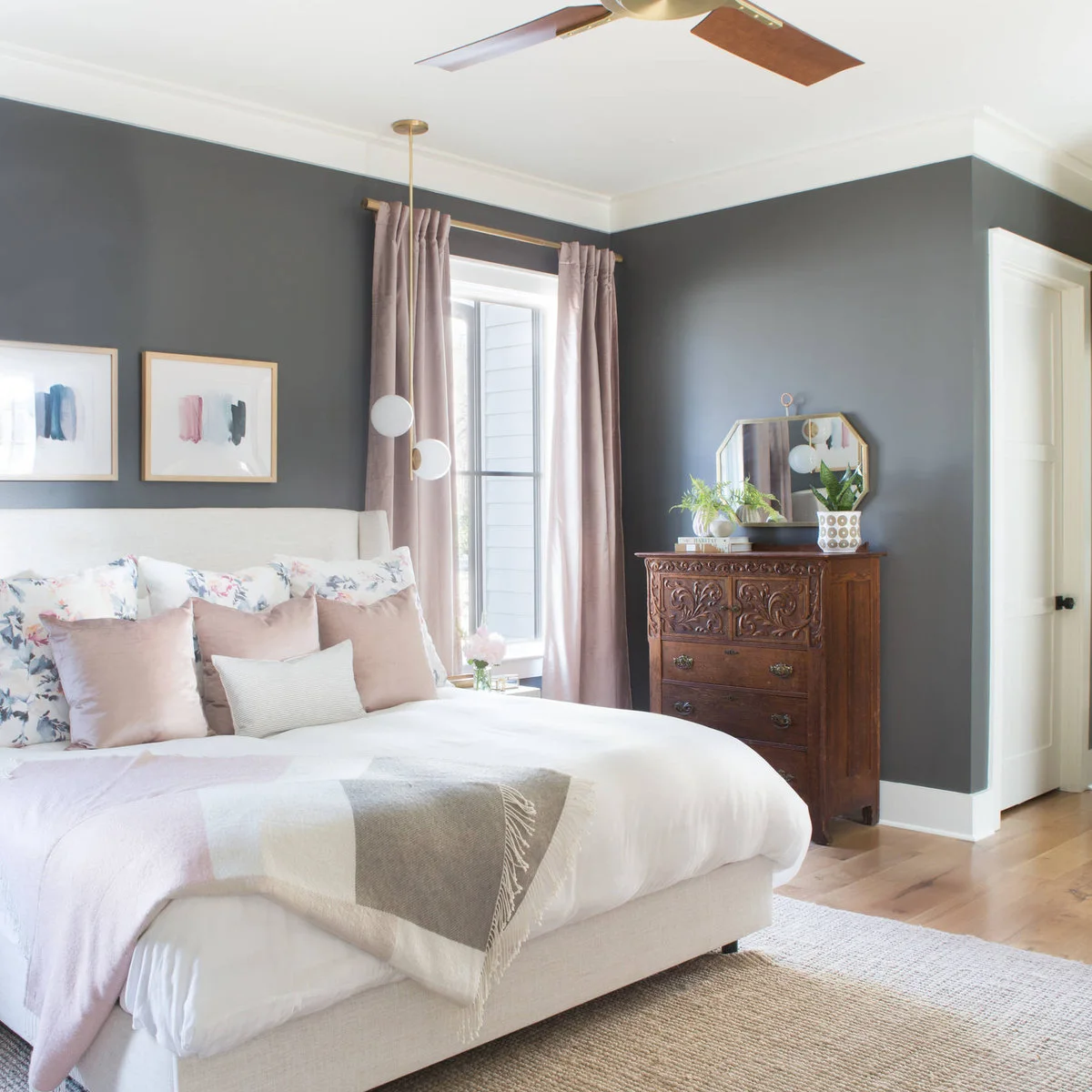 Deep grey bedroom walls with muted pink curtains, white bedding and a carved wood chest