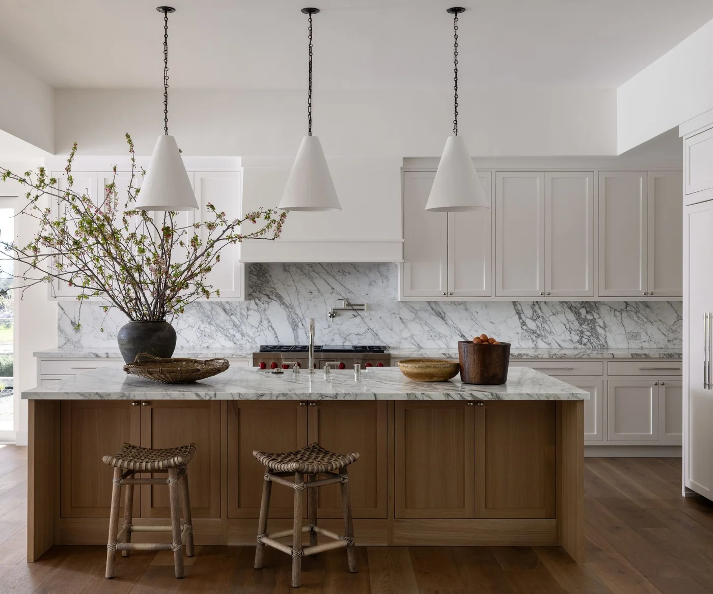 White Shaker-style cabinets with small round knobs surround a wood island beneath three white pendants.