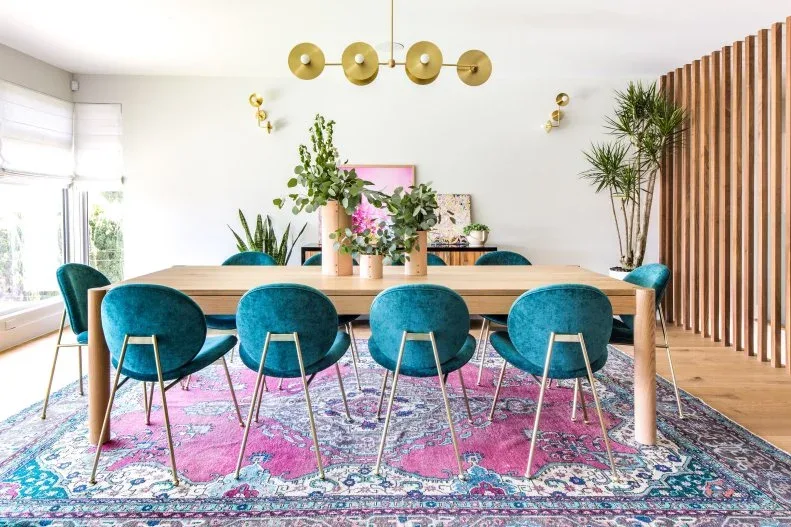 Vertical wood slats beside a long dining table with teal chairs and a pink patterned rug