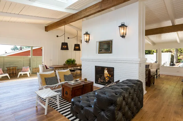 A dark tufted sofa shares a pale room with a timber chair beside a light fireplace.