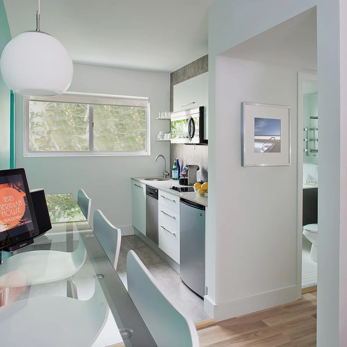 White recessed kitchenette with a sink, microwave, undercounter refrigerator and nearby desk