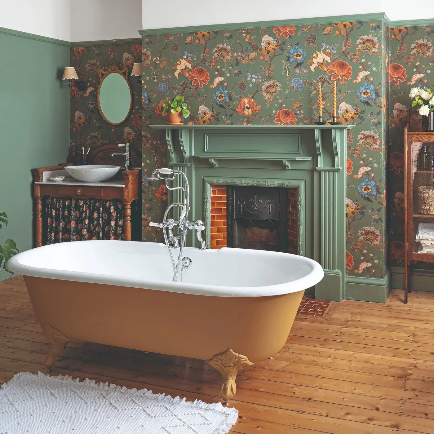 A green-painted fireplace and floral wallpaper stand behind a freestanding bath with a warm-colored outer finish.