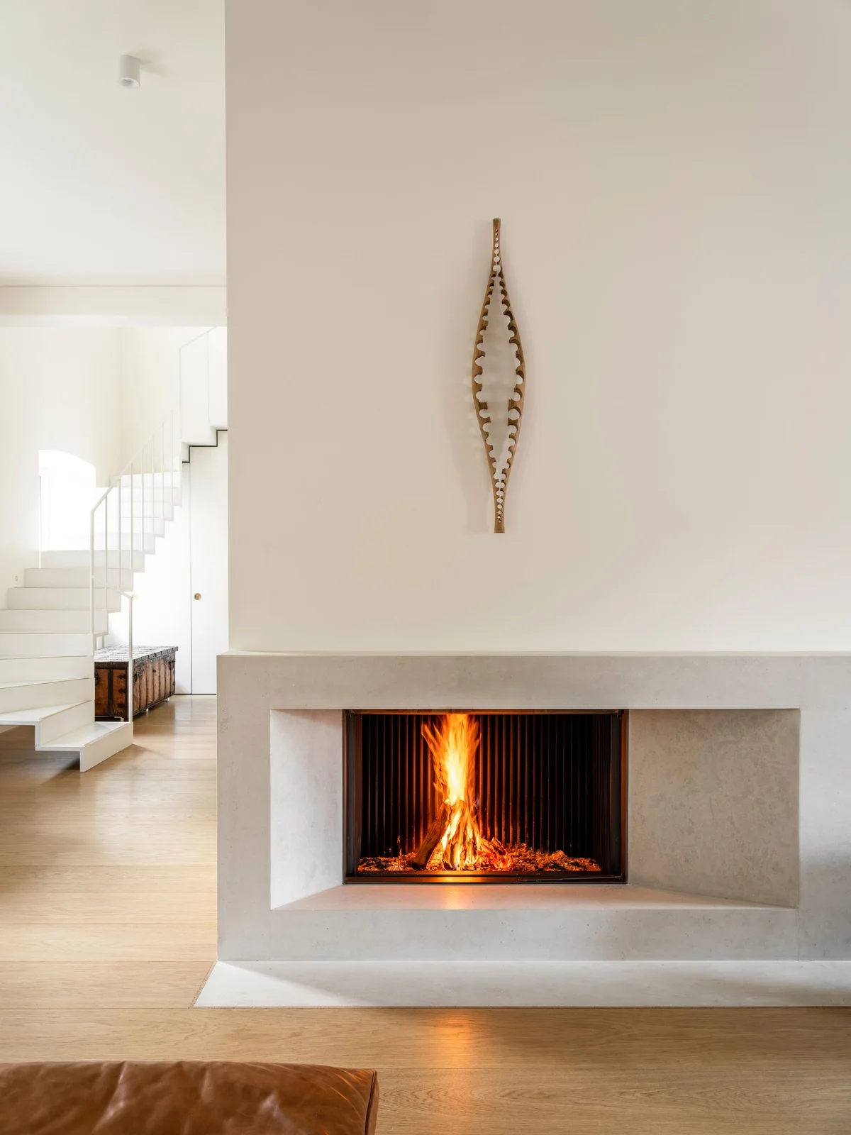 A rectangular dark fire opening sits within a broad pale recessed surround beneath a mostly clear tall wall and one narrow decorative object