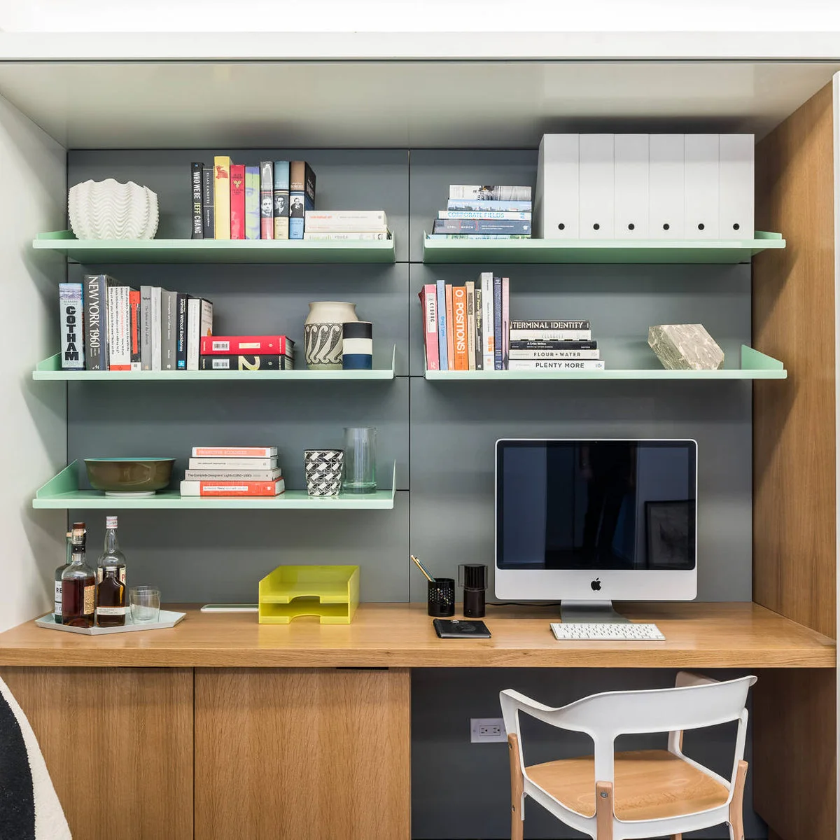 Apartment desk with green-edged shelves holding books and white file boxes above a wood counter