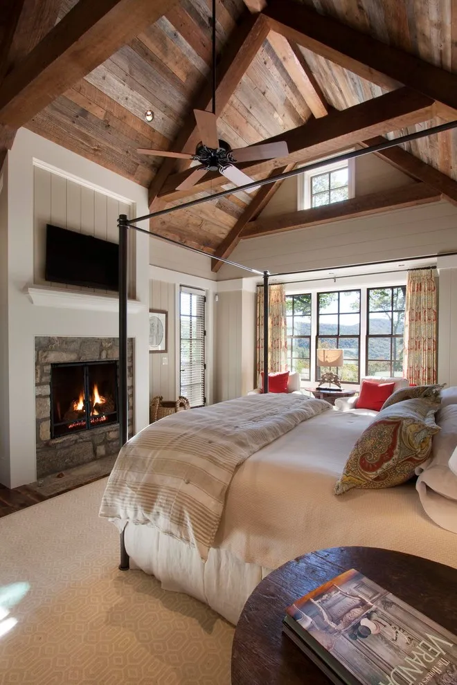 Beige bedding sits beneath a substantial timber ceiling beside a stone fireplace